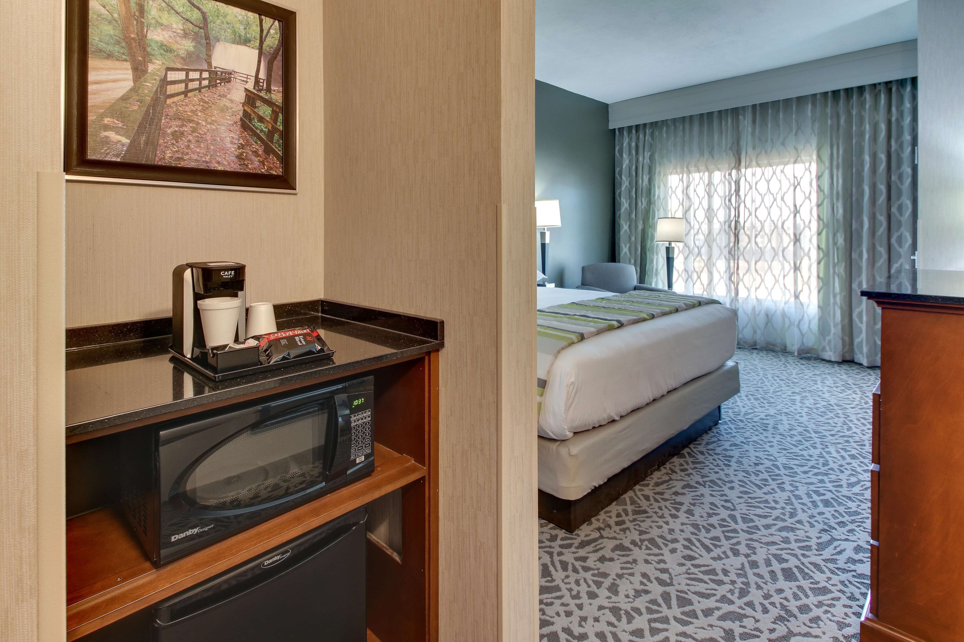 Ein Hotelzimmer mit einem Bett, einem Schreibtisch mit Mikrowelle, einer Kaffeemaschine und einem gerahmten Bild an der Wand.