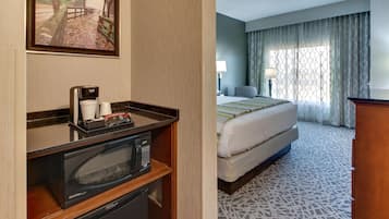 Habitación de hotel con cama, escritorio con microondas, cafetera y un cuadro en la pared.
