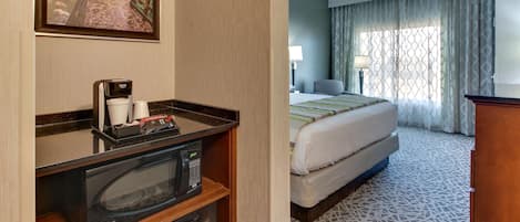 A hotel room with a bed, a desk with a microwave, a coffee maker, and a framed picture on the wall.