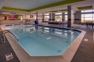 Piscina interior com sinalização clara, cadeira de salva-vidas e vista para o exterior.