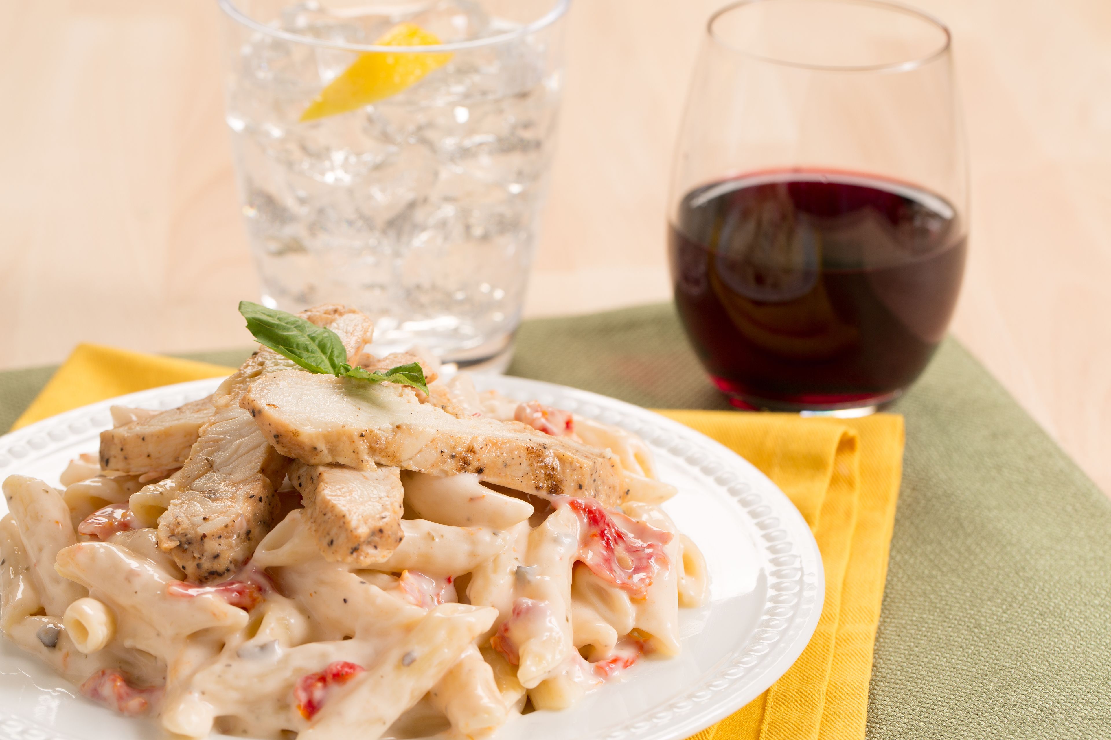 A plate of pasta with chicken and a glass of red wine.