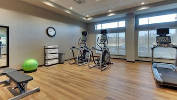 A gym with treadmills, elliptical machines, a stationary bike, a green exercise ball, and a bench.