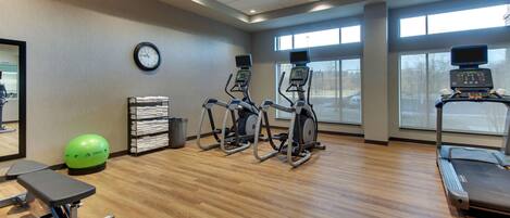 A gym with treadmills, elliptical machines, a stationary bike, a green exercise ball, and a bench.