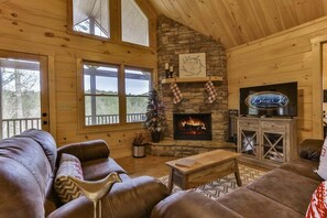 A cozy cabin interior with a stone fireplace, leather couches, and a television.