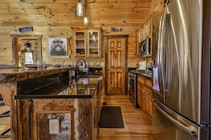 A wooden cabin interior with a kitchen featuring a large refrigerator, wooden cabinets, and a central island with a sink.