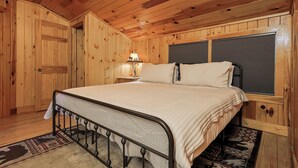 A wooden-paneled room with a bed, a nightstand, a lamp, and a window with blinds. - Cartecay Canoe House | Ellijay, GA (Ellijay)