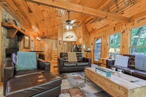 A cozy log cabin interior with leather sofas, a wooden coffee table, and a stone fireplace.