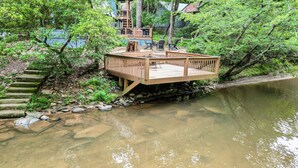 A wooden deck over a river with steps leading down to the water, surrounded by greenery. - Cartecay Canoe House | Ellijay, GA (Ellijay)