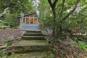 A small cabin with a wooden staircase leading up to it, surrounded by dense forest.