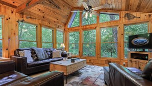 A cabin with a wooden interior, a leather sofa, a coffee table, and a television. - Cartecay Canoe House | Ellijay, GA (Ellijay)