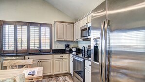 A kitchen with wooden cabinets, stainless steel appliances, and a window with blinds.