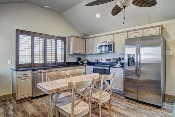 A kitchen with a dining table, chairs, stainless steel appliances, and a ceiling fan.