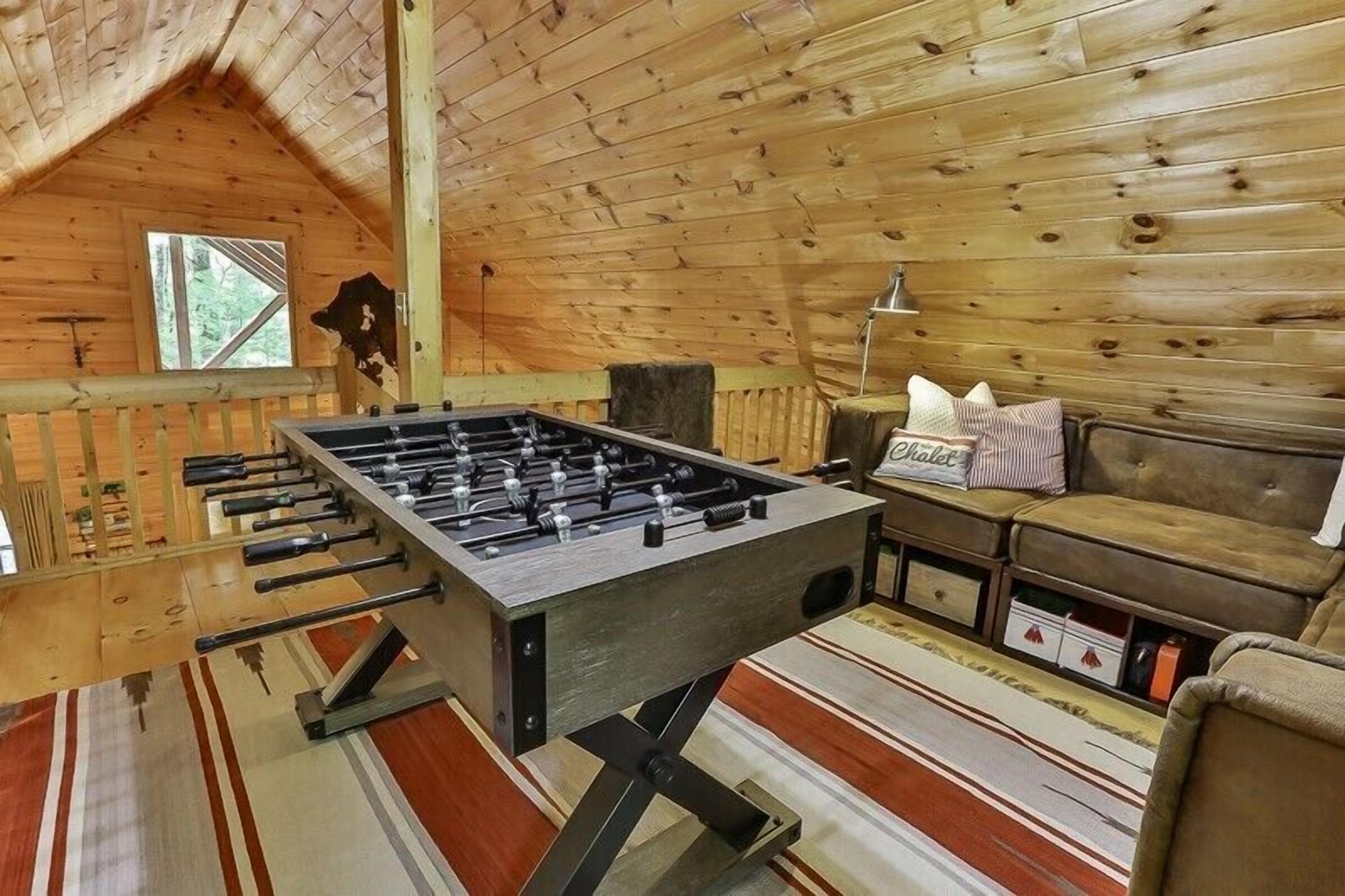 Um quarto aconchegante com uma mesa de futebol, um sofá e uma janela.