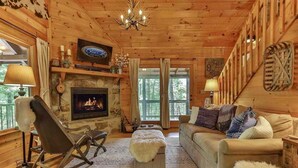 A cozy cabin interior with a fireplace, wooden walls, a sofa, a rocking chair, and a television. - Aska Retreat | Blue Ridge, GA (Cherry Log)