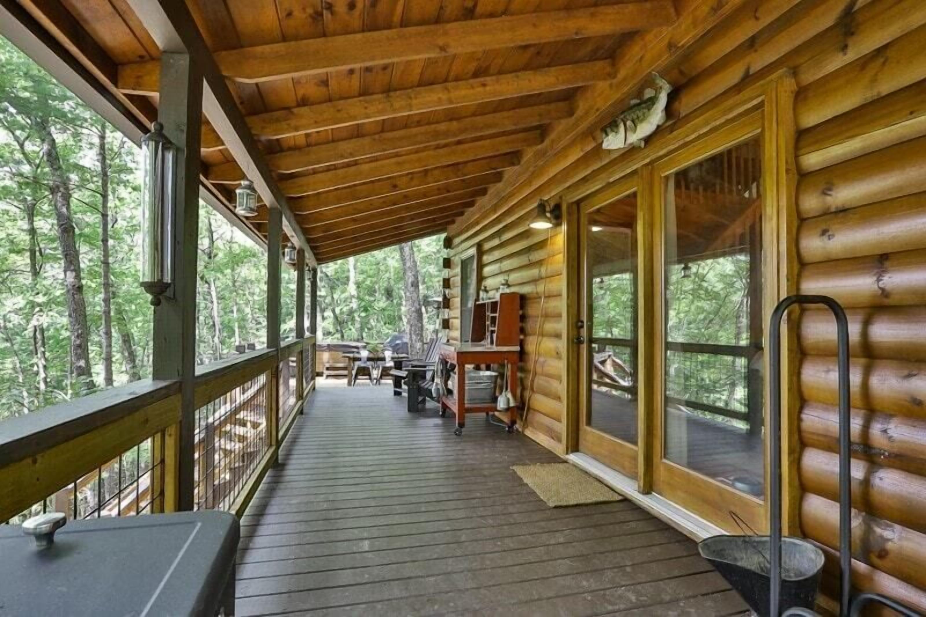 Una cabaña de madera con un porche cubierto, ventanas amplias y vistas al bosque.