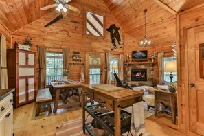 L’intérieur d’un chalet en bois comprend une table à manger, un banc, une cheminée et un ventilateur de plafond.