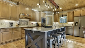 Una cocina moderna con armarios de madera, una isla central con taburetes, electrodomésticos de acero inoxidable e iluminación colgante.