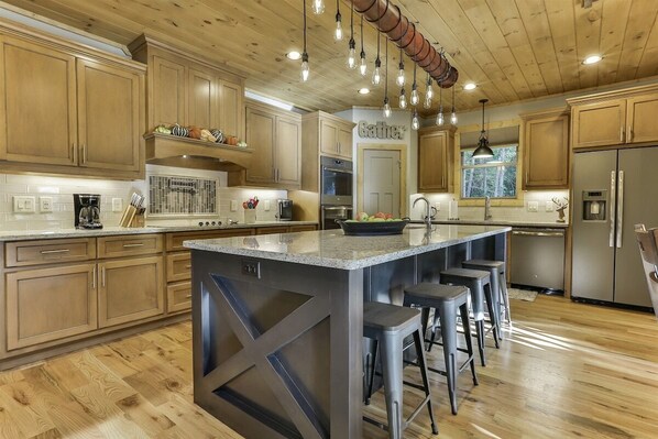A modern kitchen with wooden cabinets, a central island with stools, stainless steel appliances, and pendant lighting.