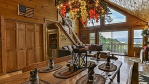 A wooden interior with a dining table set with placemats and candles, a staircase, and a view through large windows. - Mountain Lake Escape | Ellijay, GA (Ellijay)