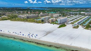 Luchtbeeld van een kustresort met meerdere hotelgebouwen, een groot zandstrand en helder turquoise water.
