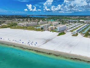 Vista aérea de un complejo turístico costero con varios edificios de hotel, una amplia playa de arena y aguas turquesas cristalinas.