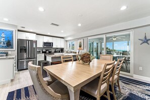 A modern kitchen with stainless steel appliances, a dining area with a wooden table and chairs, and a view through glass doors to an outdoor patio.