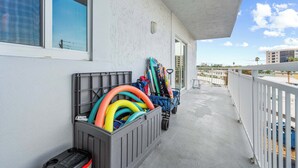 Un balcon orné d’une rangée de tuyaux d’arrosage multicolores et d’un chariot, un immeuble à la façade blanche et un ciel dégagé.