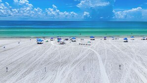 Een strand met helderblauw water, wit zand en blauwe parasols.