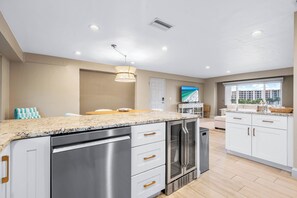A modern kitchen with a granite countertop, stainless steel appliances, and a large window offering a view of the city. - Beachfront 2BR condo w/ private beach access & views (Siesta Key)
