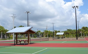Una cancha de tenis con pabellón, mesas de picnic y farolas.