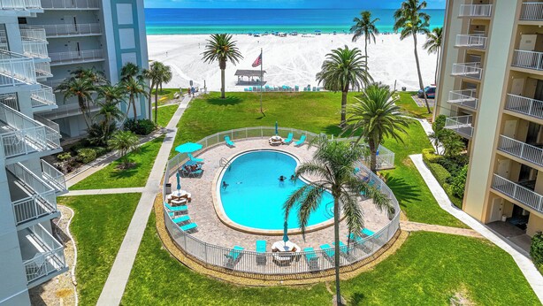 Een hotel met een zwembad, uitzicht op het strand en palmbomen.