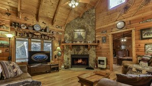 A cabin interior with a stone fireplace, wooden walls, a television, and a cozy seating area. - River Run | Ellijay, GA (Ellijay)
