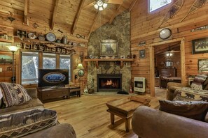 L’intérieur d’une cabane est agrémenté d’une cheminée en pierre, de murs en bois, d’un téléviseur et d’un coin salon confortable.