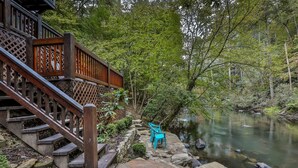 A wooden staircase leading to a stone pathway beside a calm river, with a wooden fence and a bench. - River Run | Ellijay, GA (Ellijay)