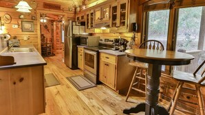 A wooden cabin interior with a kitchen, dining table, and a view of the outdoors. - River Run | Ellijay, GA (Ellijay)