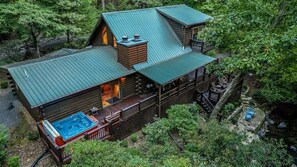A cabin with a hot tub, deck, and a view of the surrounding forest. - River Run | Ellijay, GA (Ellijay)