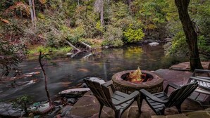 A stone fire pit with chairs, a river, and a forested area. - River Run | Ellijay, GA (Ellijay)