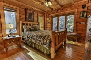 A wooden cabin bedroom with a bed, dresser, and windows. - River Run | Ellijay, GA (Ellijay)