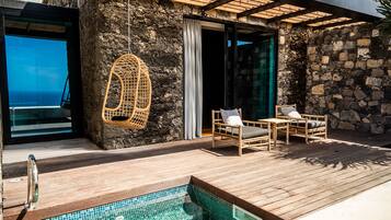 Una terraza de madera con piscina, sillas de mimbre y un muro de piedra.
