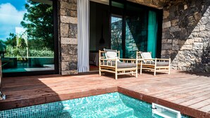 A wooden deck with a swimming pool, two wicker chairs, and a stone wall. - Sensi Azores Nature and SPA (Ponta Delgada)