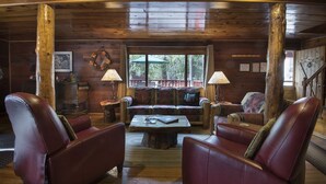 Interior acolhedor de uma cabana com paredes de madeira, um sofá, poltronas de couro e uma mesa de centro.