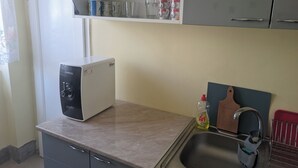 Een keuken met een inbouwmagnetron, een spoelbak en een plank boven het aanrecht.