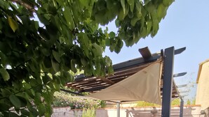 Ulkoterassi, jossa on kivilaattalattia, pergola ja sen yllä oleva katos sekä istuimia.
