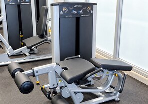 A leg curl and leg extension machine in a gym with a bench and safety warnings. - 4 Px partial sea view, - Rent.Apart.Hollywood (Hollywood)