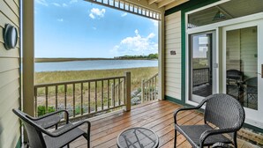 A covered deck with wicker chairs and a table, overlooking a body of water.