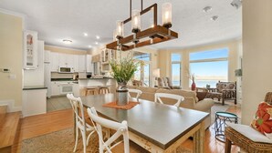 A spacious kitchen with white cabinets, a dining area with a large table, and a view of the ocean through large windows.
