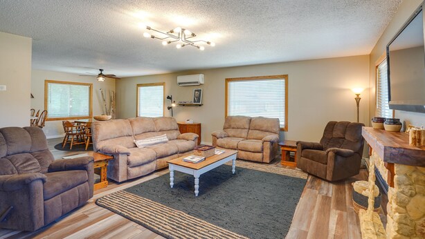 A living room with beige walls, a ceiling fan, a fireplace, and a dining area with wooden furniture. - Roosevelt Suite of Dakota Place Lodge in Medora! (Medora)