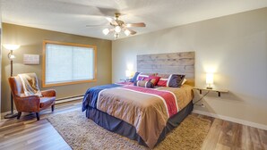 A bedroom with a bed, a chair, a ceiling fan, a window with blinds, and a wall-mounted nightstand with a lamp. - Roosevelt Suite of Dakota Place Lodge in Medora! (Medora)