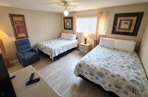 A room with two beds, a chair, a desk with a computer, a ceiling fan, and framed pictures on the walls. - Ocean Sky #1604 Closest Beach Access 2-Bd 2-Bath 2nd Floor (Destin)