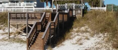 A wooden staircase leading to a beach house with a white fence and palm trees in the background.